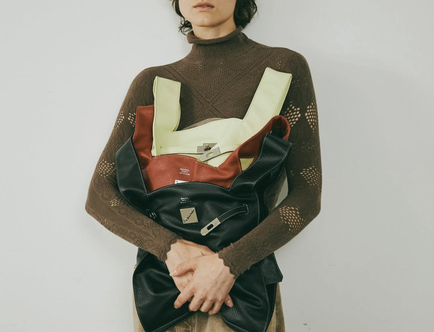 Person holding several leather handbags in different colors against a neutral background.