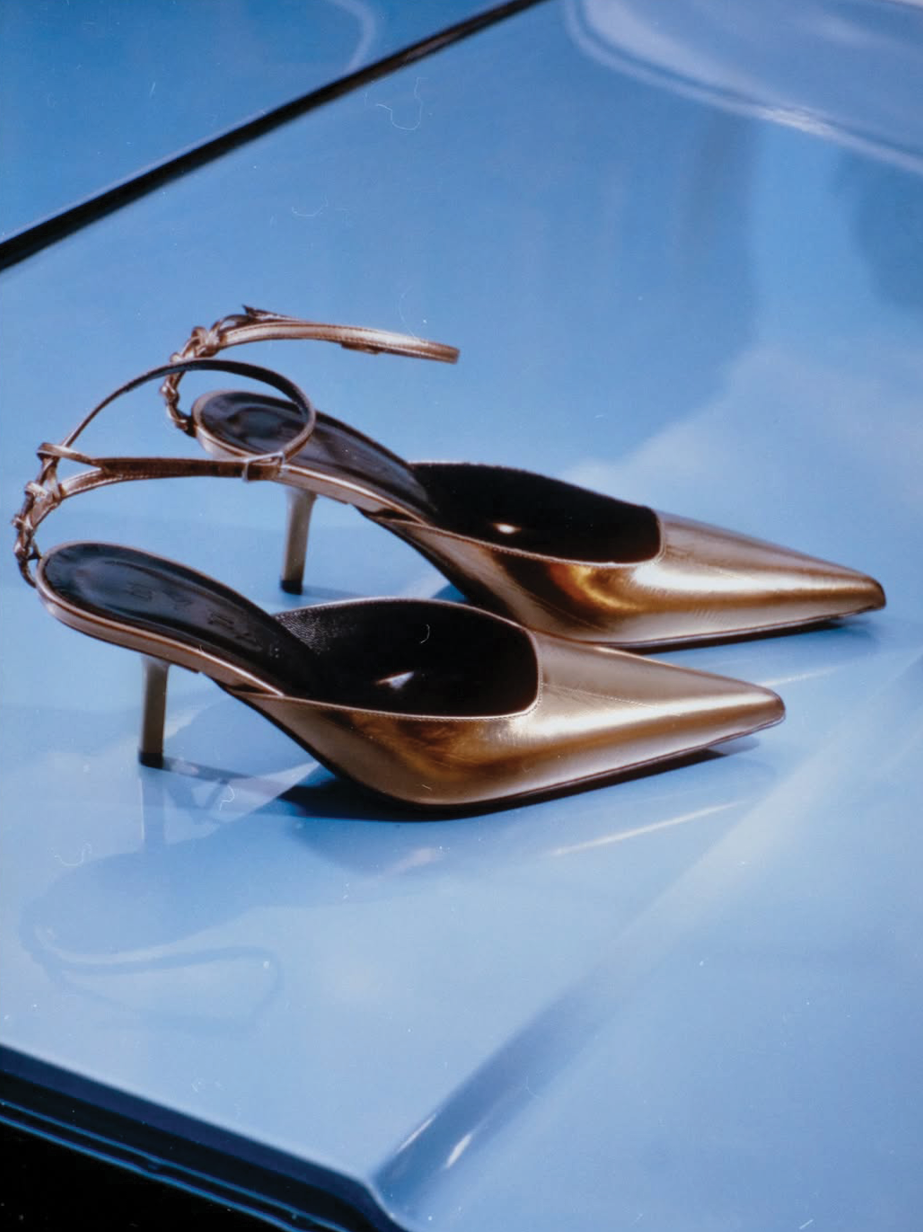 Pair of metallic gold high-heel shoes on a glossy light-blue surface.